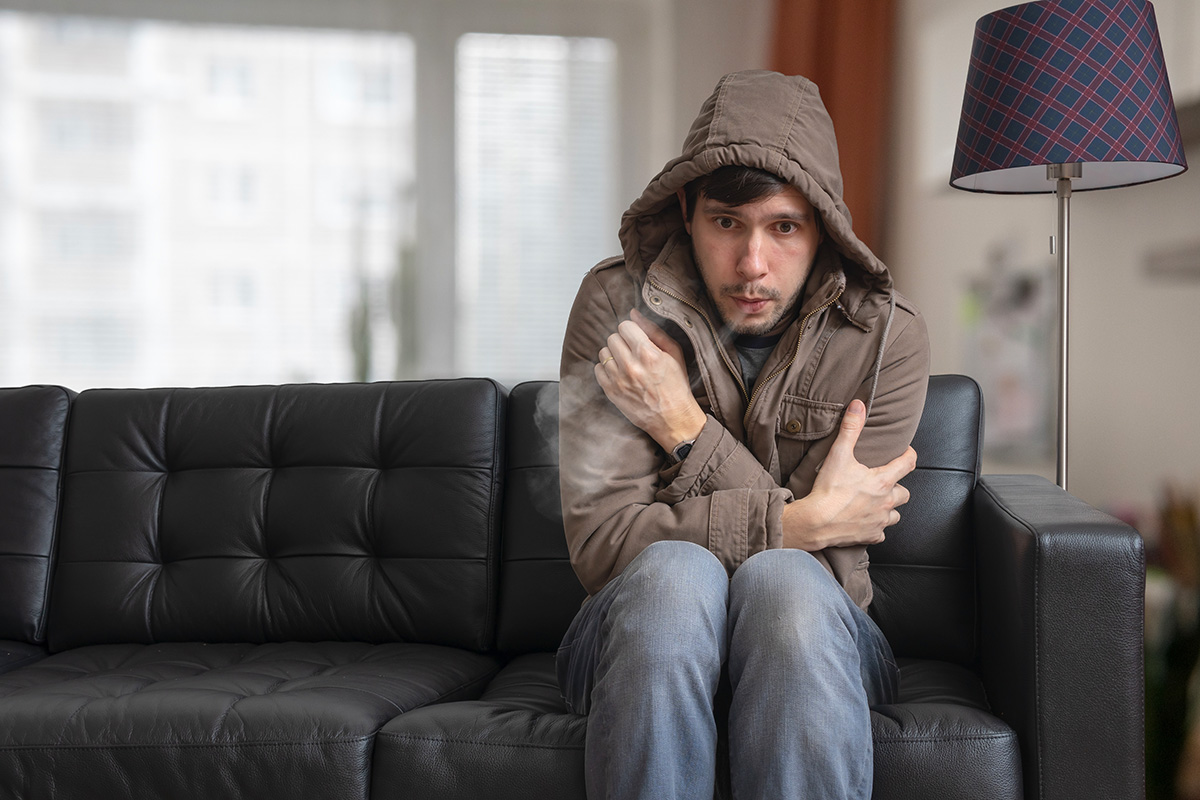 young man wearing coat shivers in a cold living room