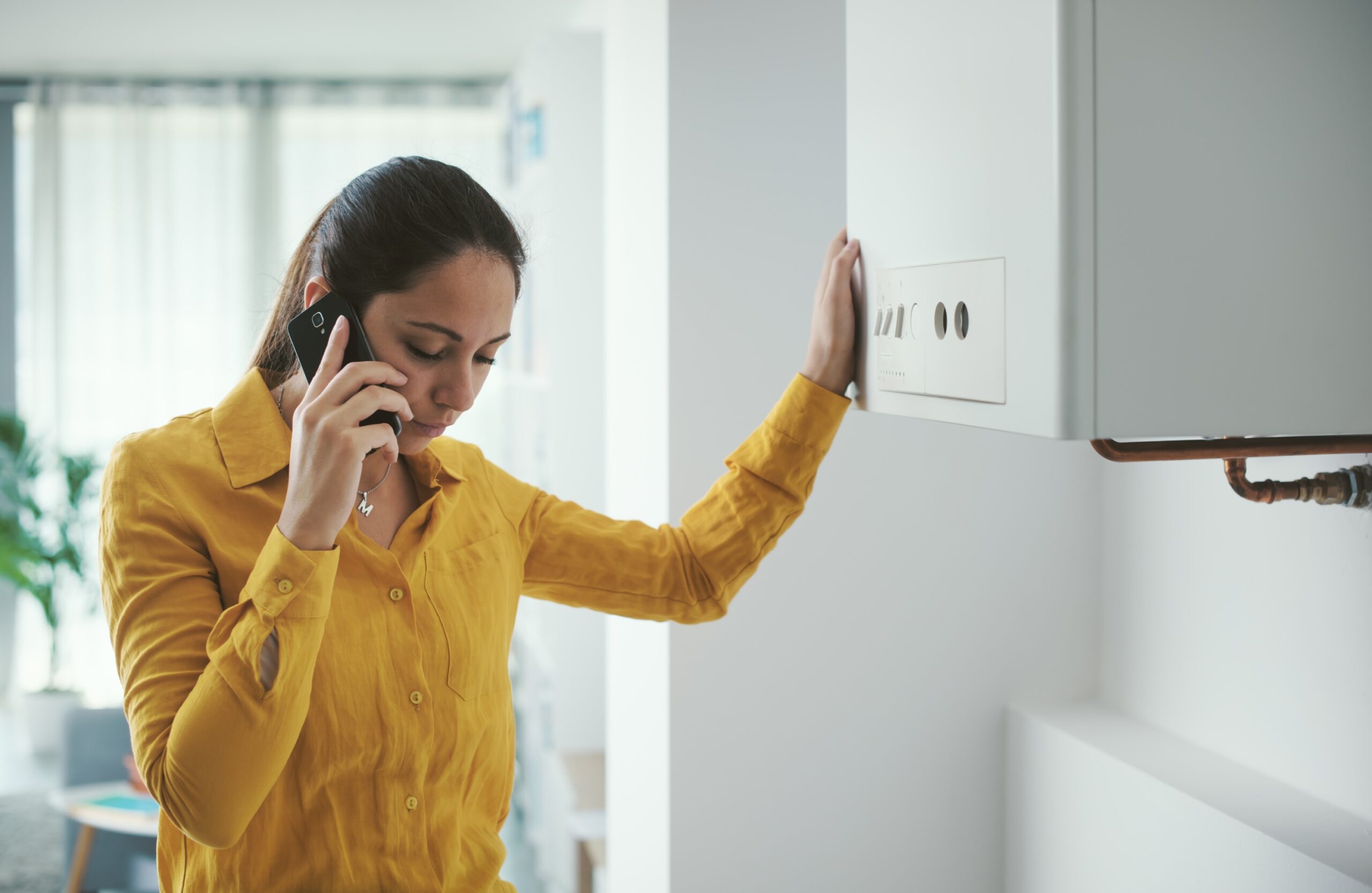 Worried woman calling an emergency service for boiler breakdown using her smartphone