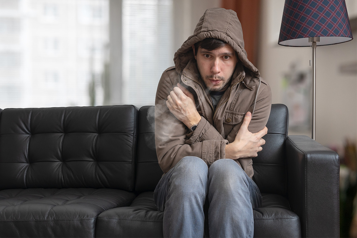 man wearing coat shivering in cold living room because heat pump is not working